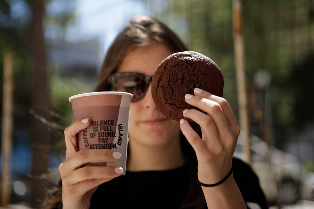 A WOMAN HOLDIND A COFFEE ISLAND'S CHOCOLATE COOKIE AND A COFFEE.